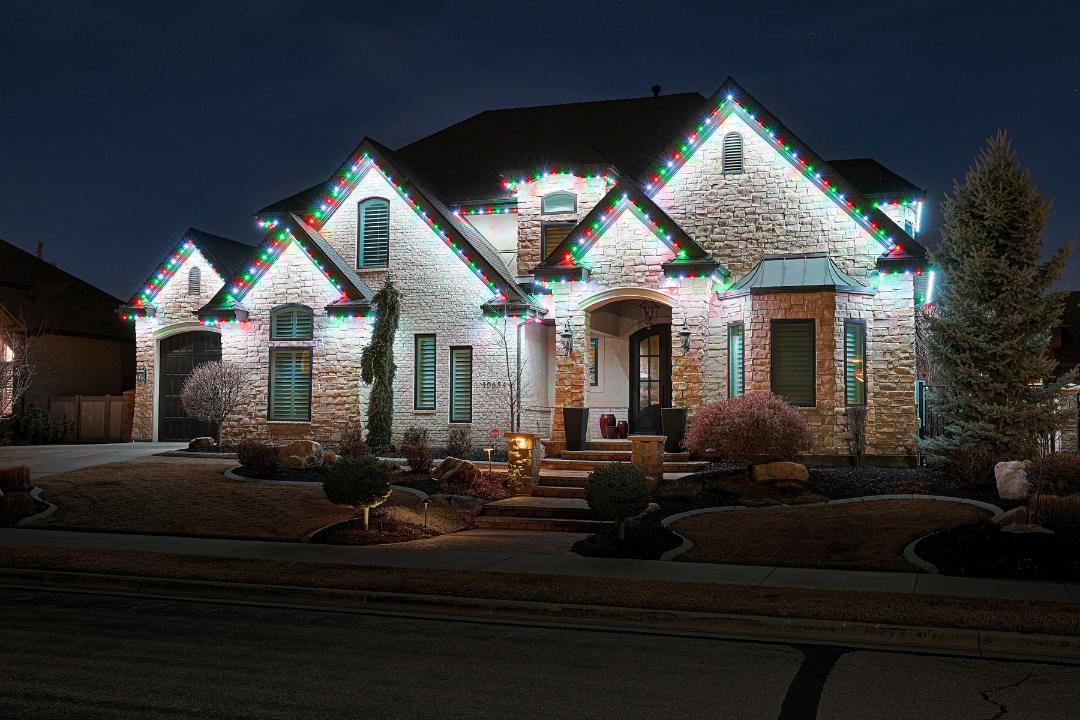 Red and green permanent holiday lights on a stone craftsman home